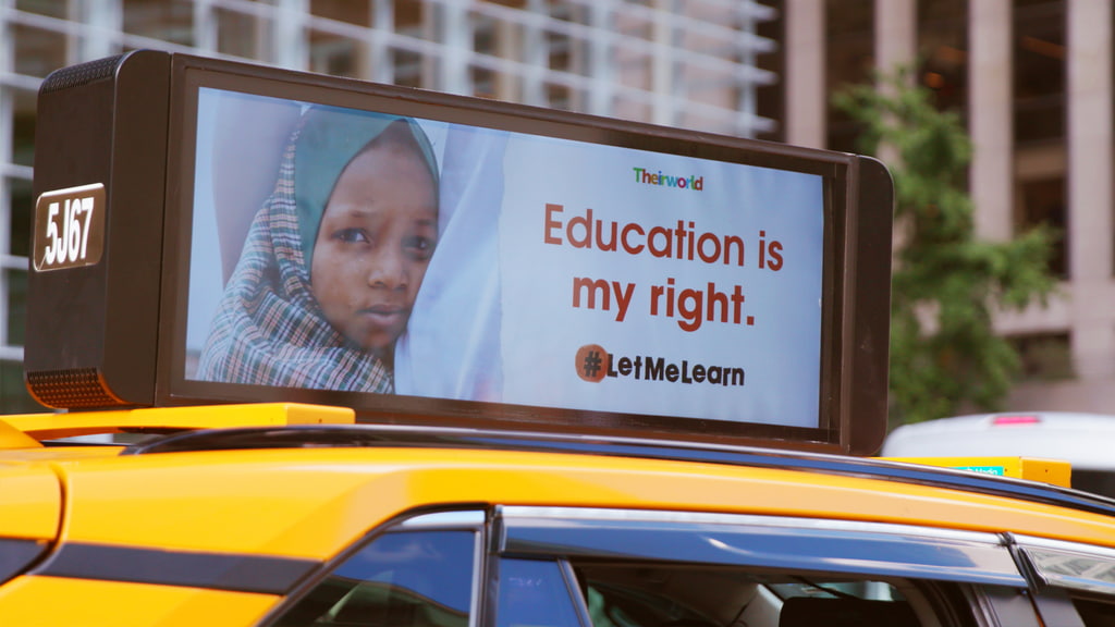 An advertisement on top of a taxi cab that features a Black child in a hijab, the Theirworld logo, a headline that reads, 