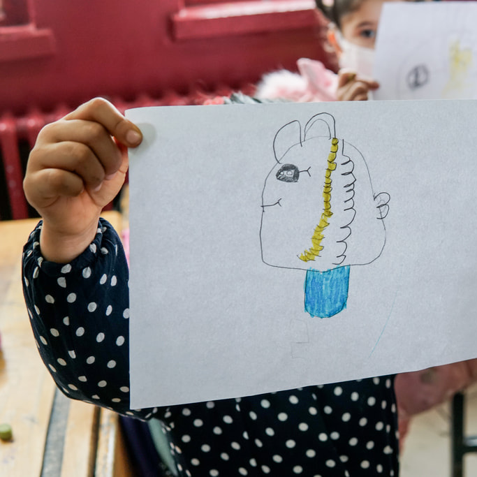 A child holds up their drawing of a fish