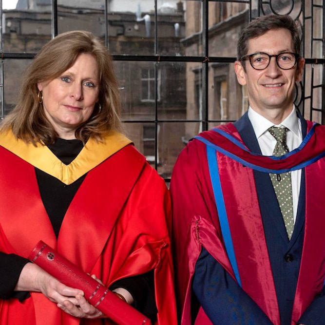Sarah Brown in graduation robes that are bright red standing next to another man in graduation robes